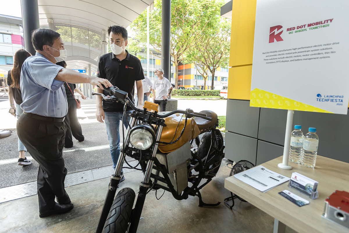 A photo of a man pointing at an electric vehicle.